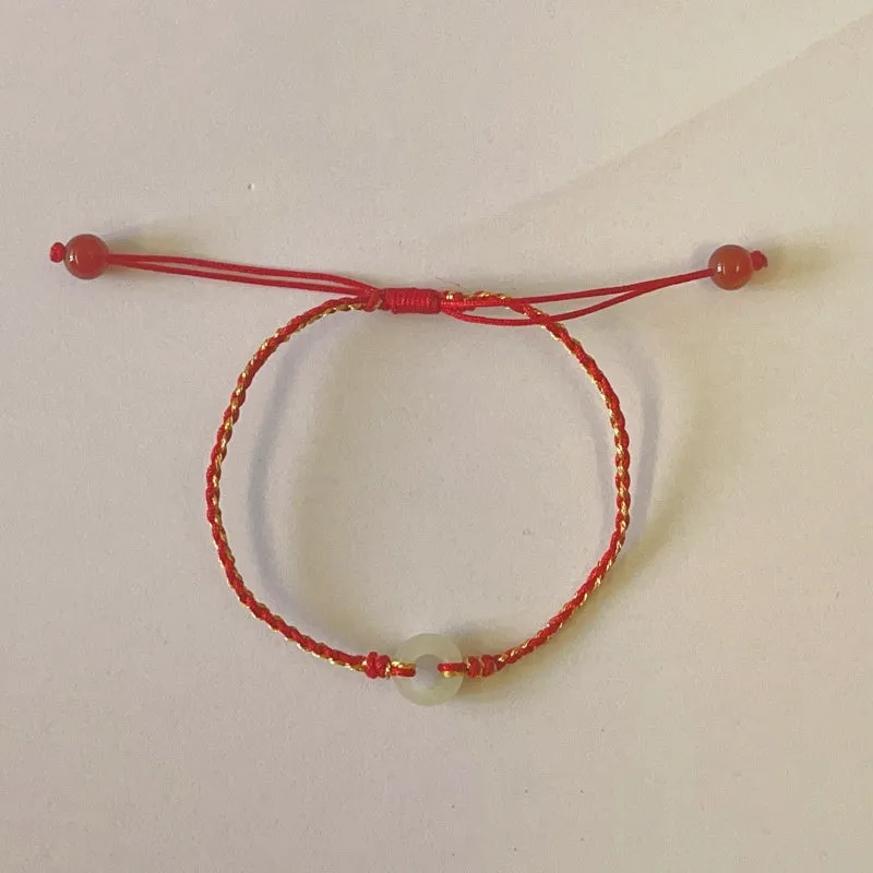 Red rope braided bracelet with natural wave-shaped Hetian jade pendant for Tiger Year birth year, on a neutral background