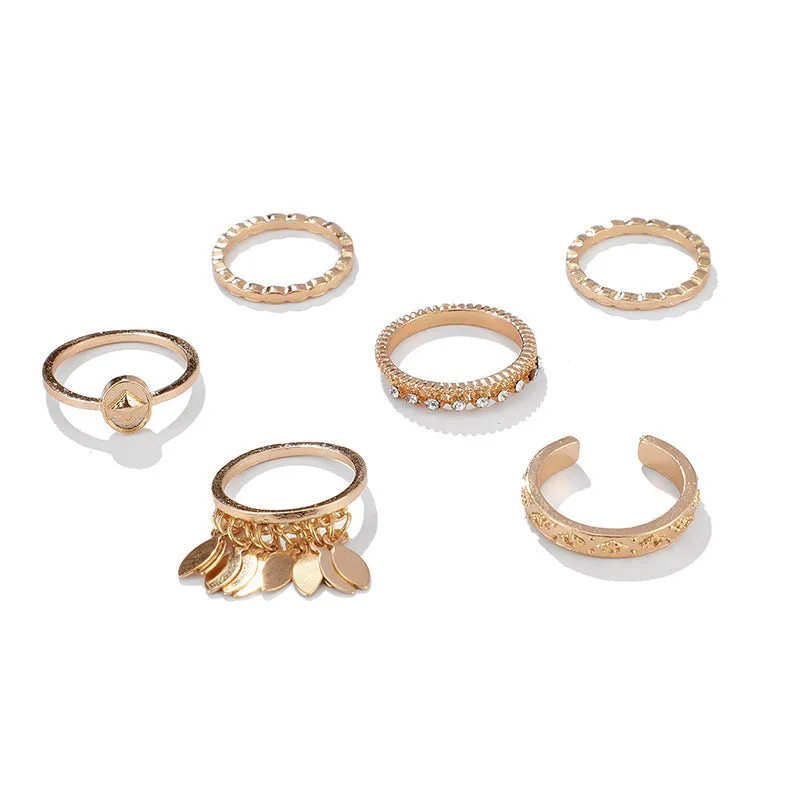 Six gold alloy rings with geometric leaf and tassel designs on a light background