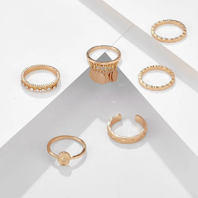 Six gold alloy rings with geometric leaf and tassel designs on a light background