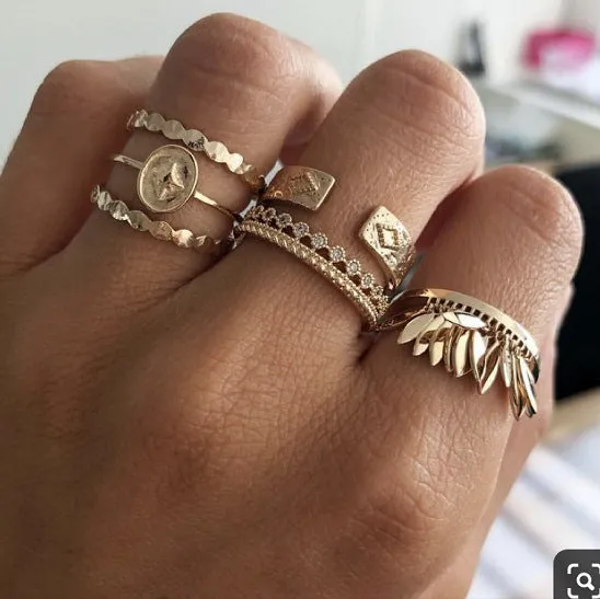 Six gold alloy rings with geometric leaf and tassel designs on a light background