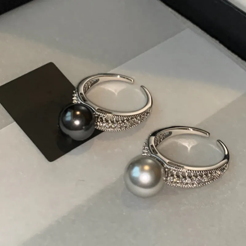 Women's adjustable copper ring with black pearl and geometric open design on an index finger.