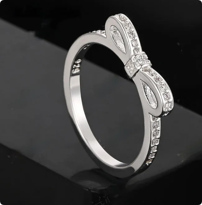 Silver coloured bow-shaped ring with sparkling rhinestone zircon crystals on a finger.