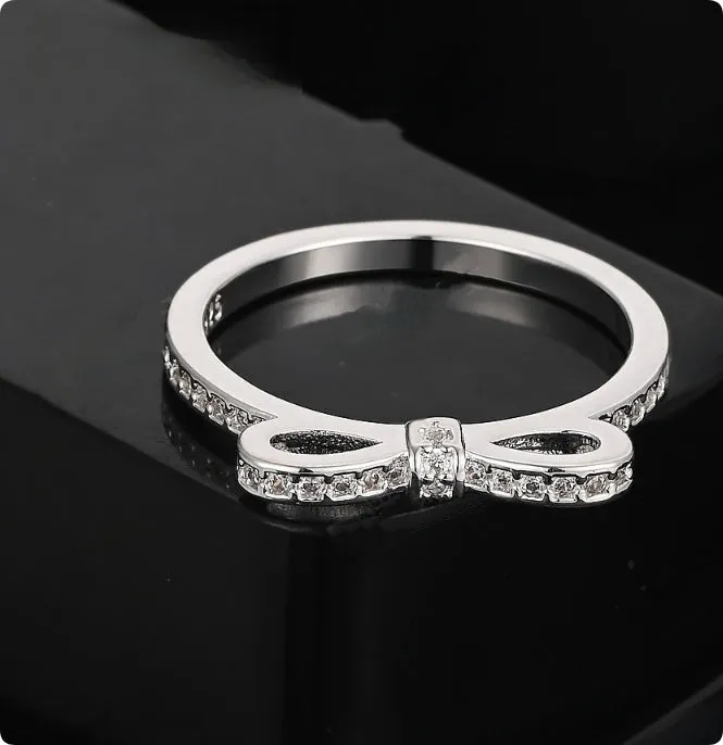 Silver coloured bow-shaped ring with sparkling rhinestone zircon crystals on a finger.