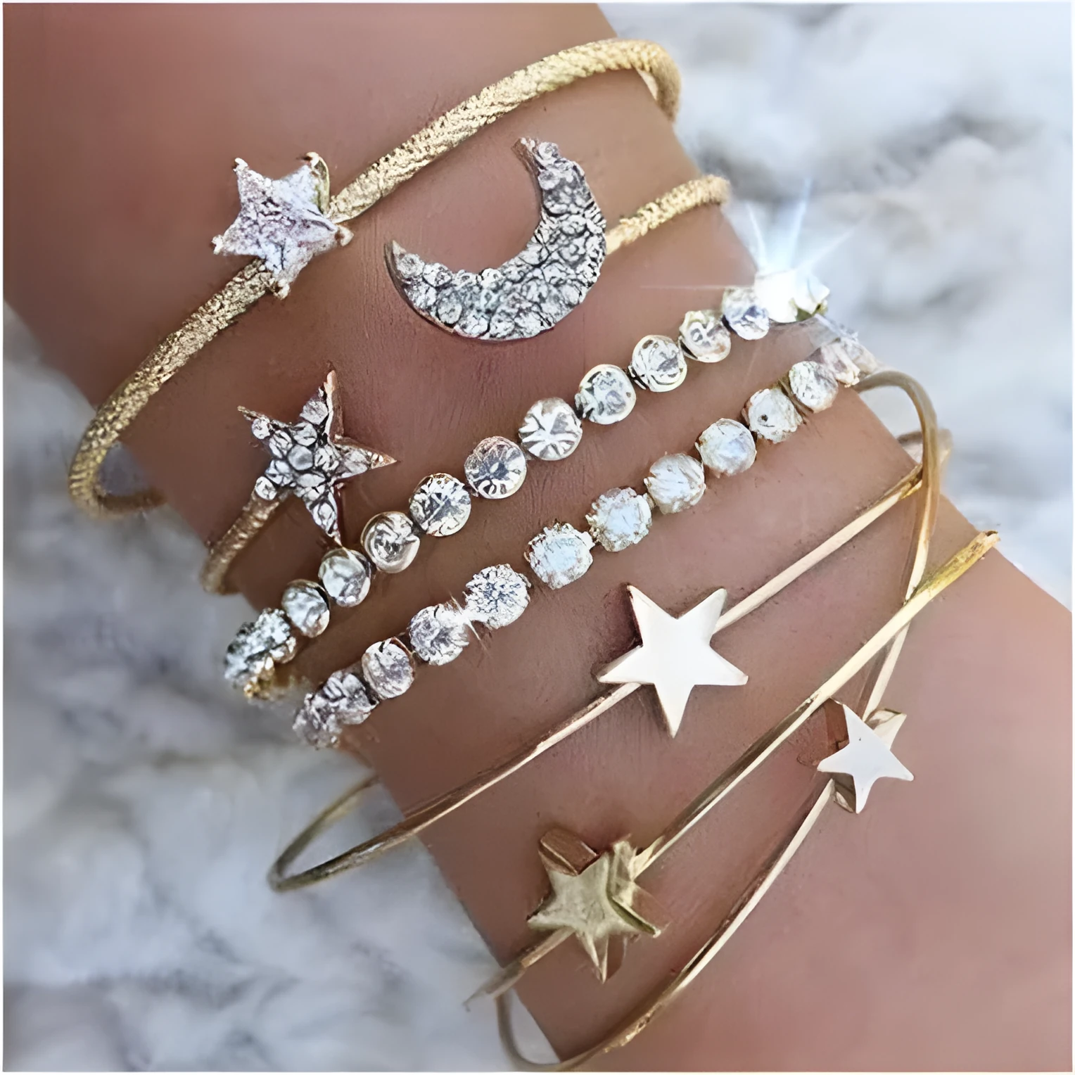 Four gold and silver metal cuff bracelets with moon and star designs on a plain background