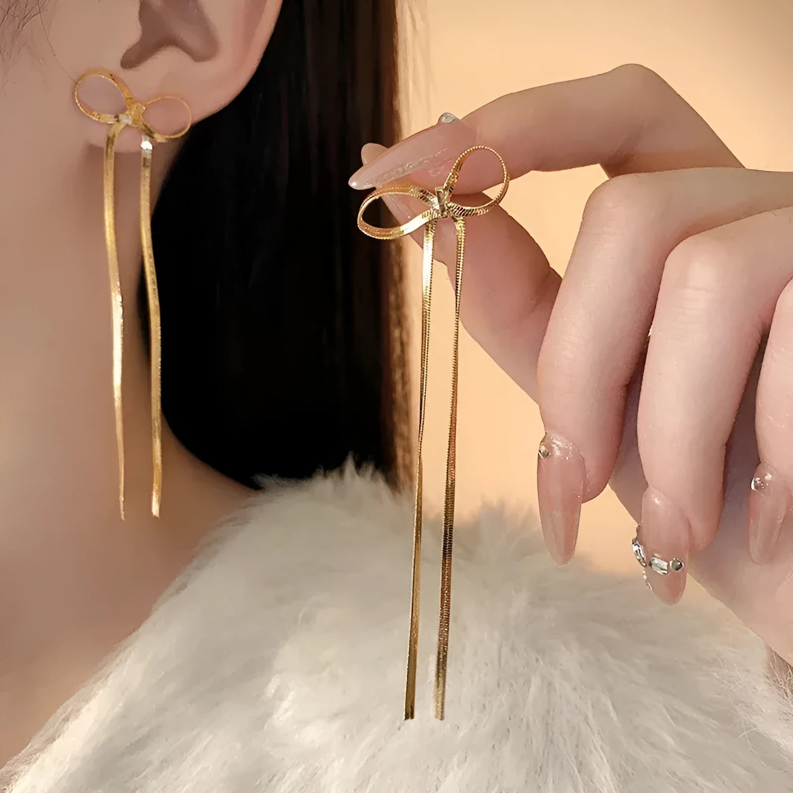 Gold plated bow ribbon dangle earrings with tassel tails on white background