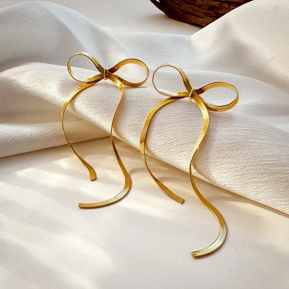 Gold plated bow ribbon dangle earrings with tassel tails on white background