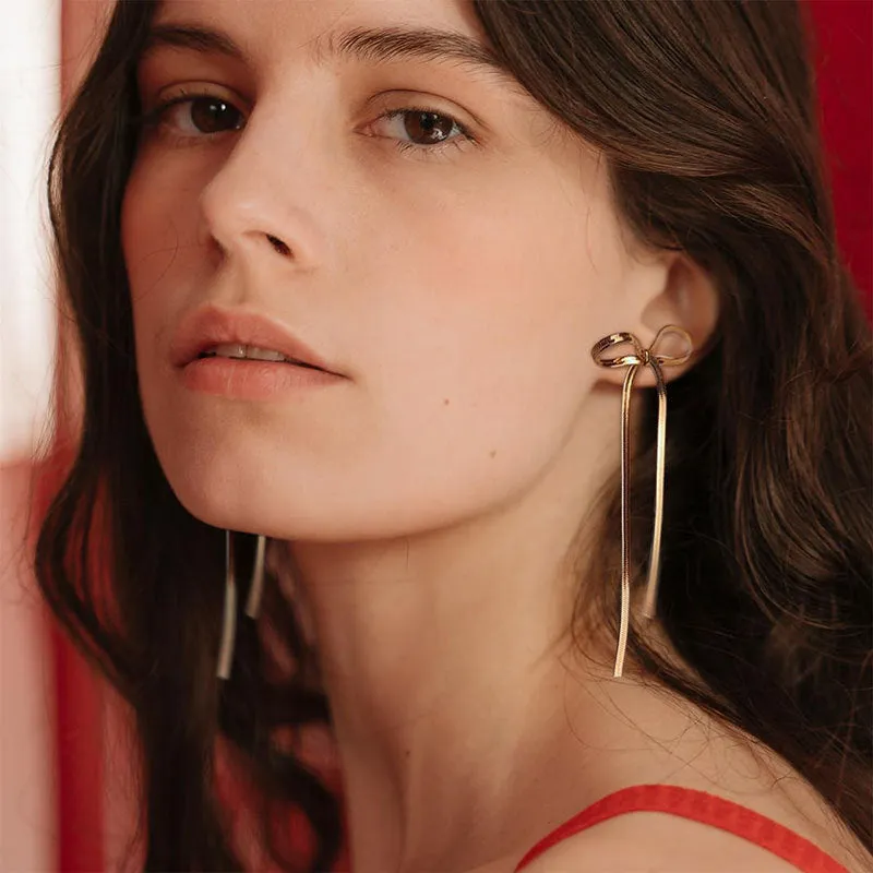 Gold plated bow ribbon dangle earrings with tassel tails on white background