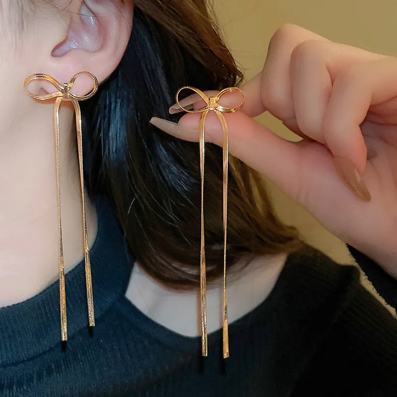 Gold plated bow ribbon dangle earrings with tassel tails on white background