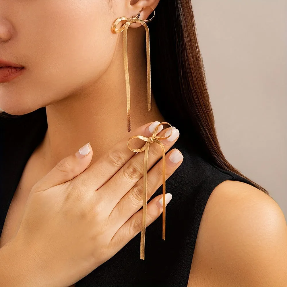Gold plated bow ribbon dangle earrings with tassel tails on white background