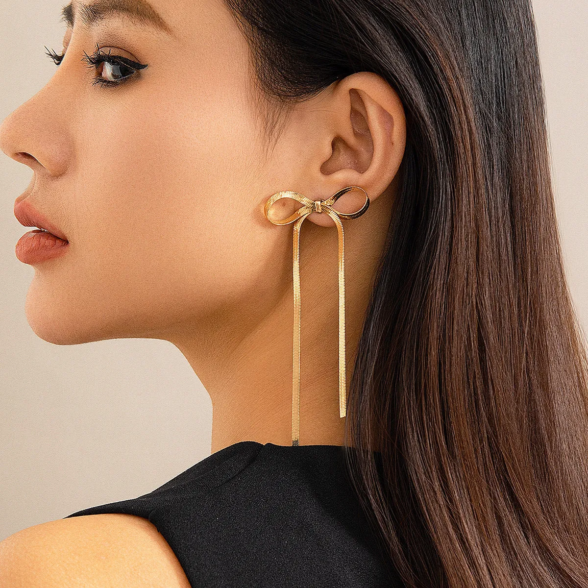 Gold plated bow ribbon dangle earrings with tassel tails on white background
