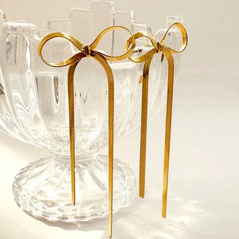 Gold plated bow ribbon dangle earrings with tassel tails on white background