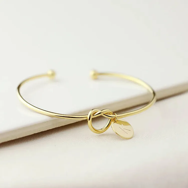 Personalised initial heart knot bracelet in gold finish with custom letter on a white background
