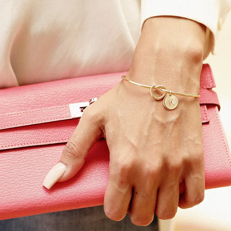 Personalised initial heart knot bracelet in gold finish with custom letter on a white background