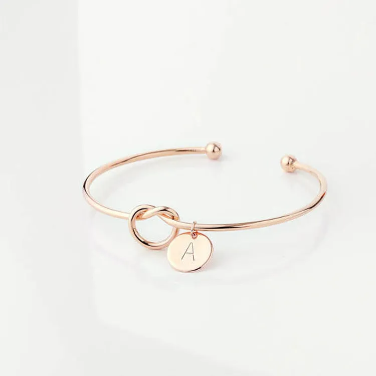 Personalised initial heart knot bracelet in gold finish with custom letter on a white background