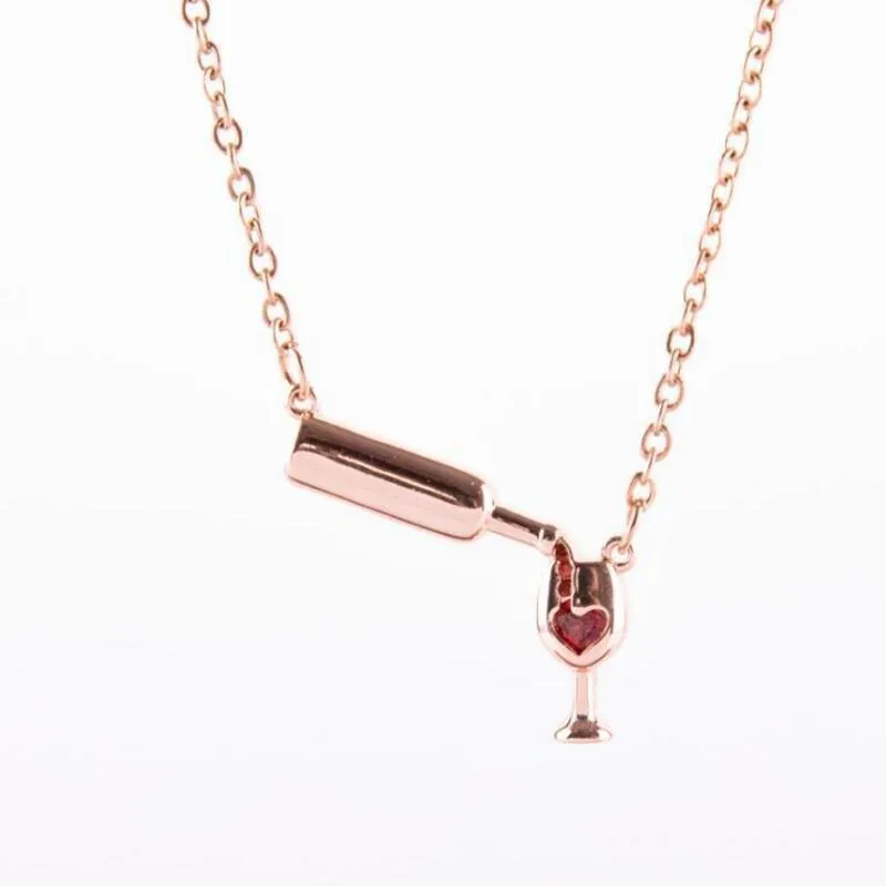 Gold alloy wine bottle and glass pendant necklace on a light background