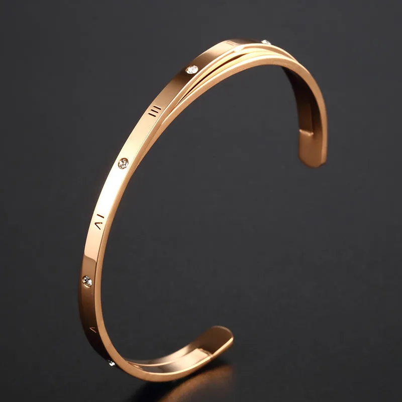 Open-ended stainless steel bracelet with inlaid zircon stones and a love charm in rose gold colour.