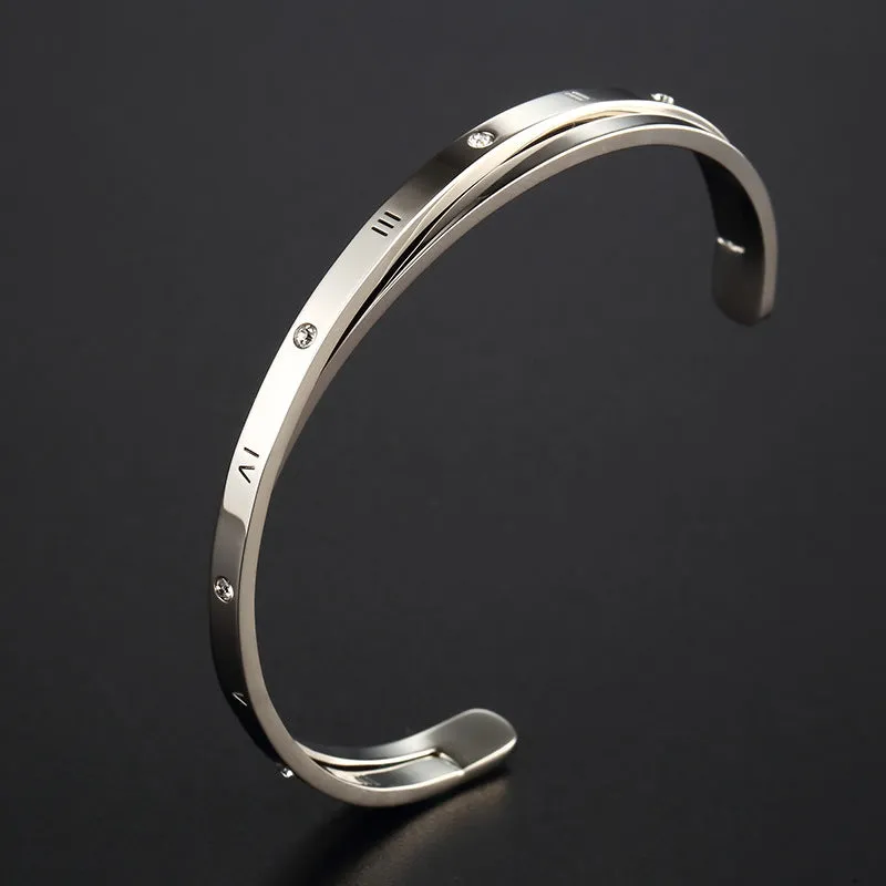 Open-ended stainless steel bracelet with inlaid zircon stones and a love charm in rose gold colour.