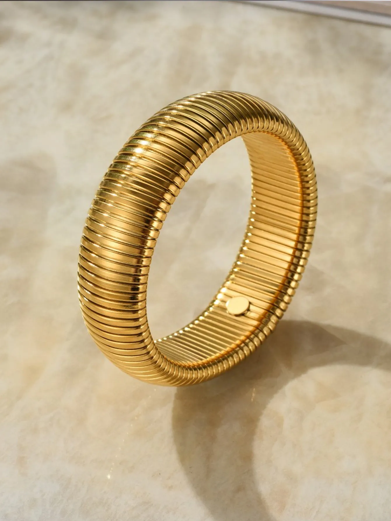 Gold women's elastic bracelet with a wide vertical stripe pattern, shown on a wrist.