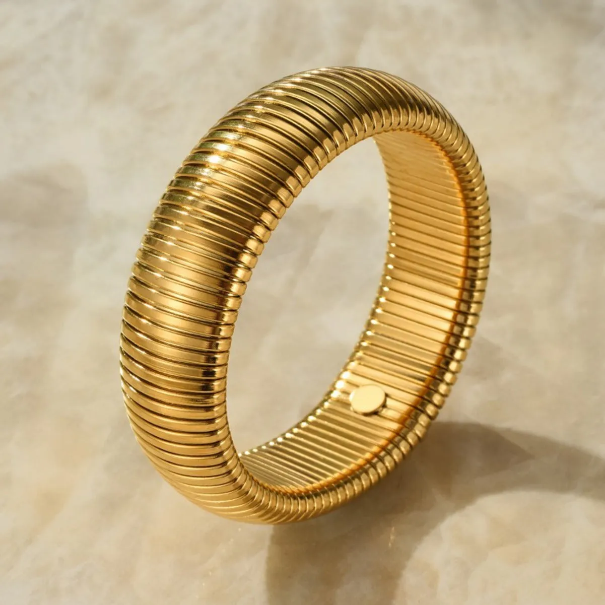 Gold women's elastic bracelet with a wide vertical stripe pattern, shown on a wrist.