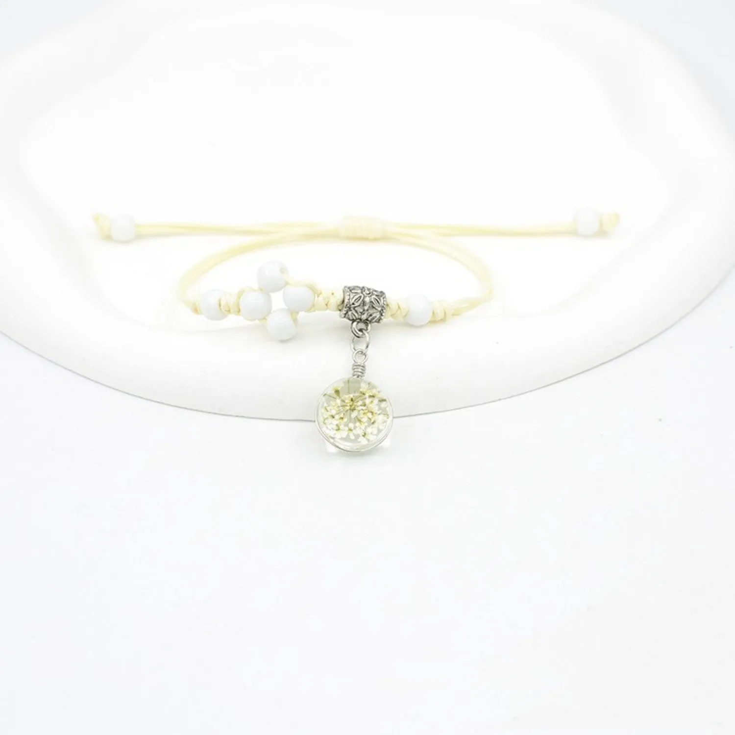 Hand-woven glass bracelet with large beads containing dried flowers and lace decorations, shown in blue.