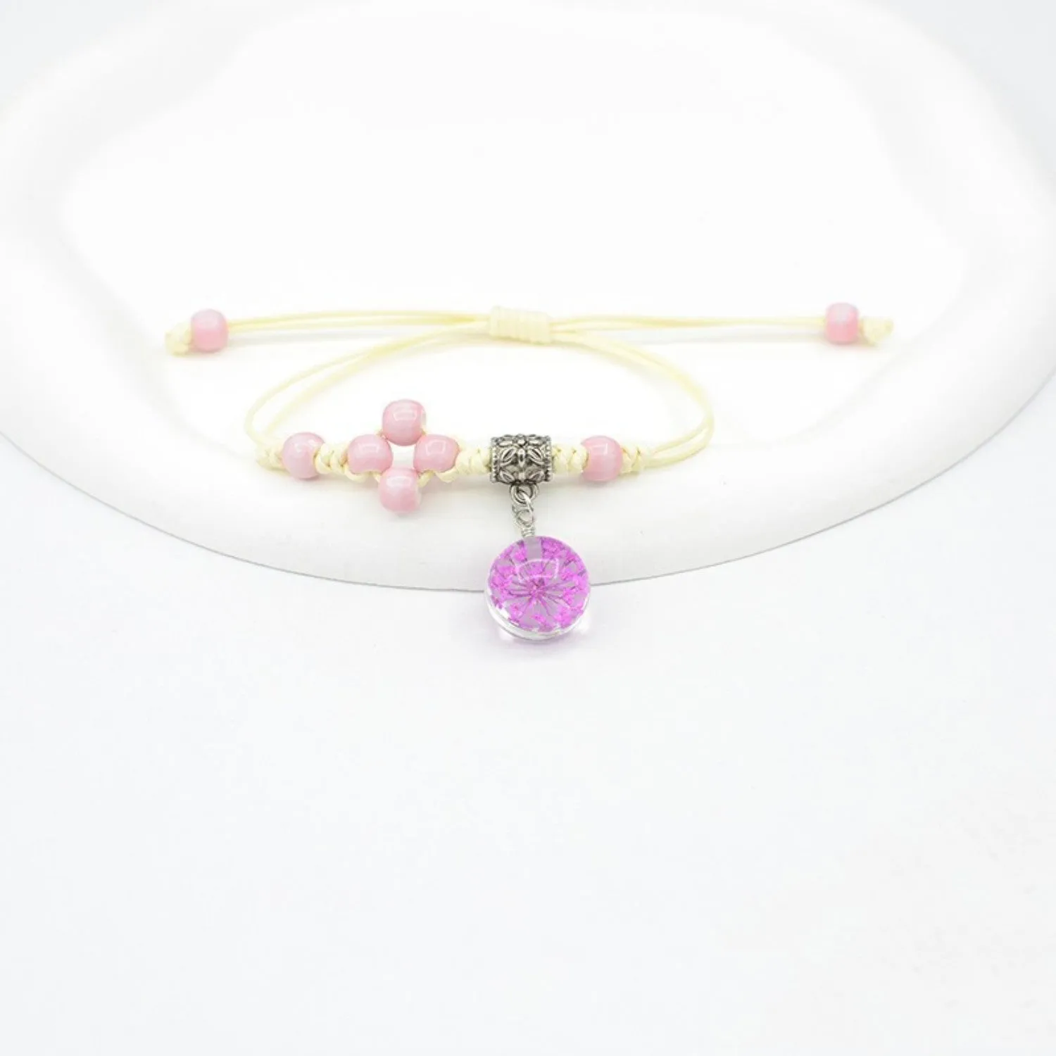 Hand-woven glass bracelet with large beads containing dried flowers and lace decorations, shown in blue.
