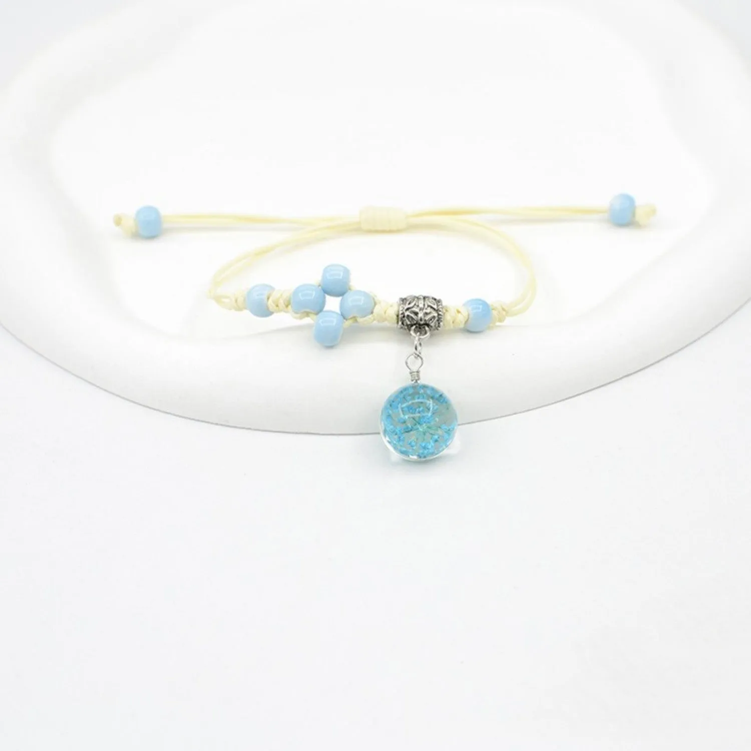 Hand-woven glass bracelet with large beads containing dried flowers and lace decorations, shown in blue.
