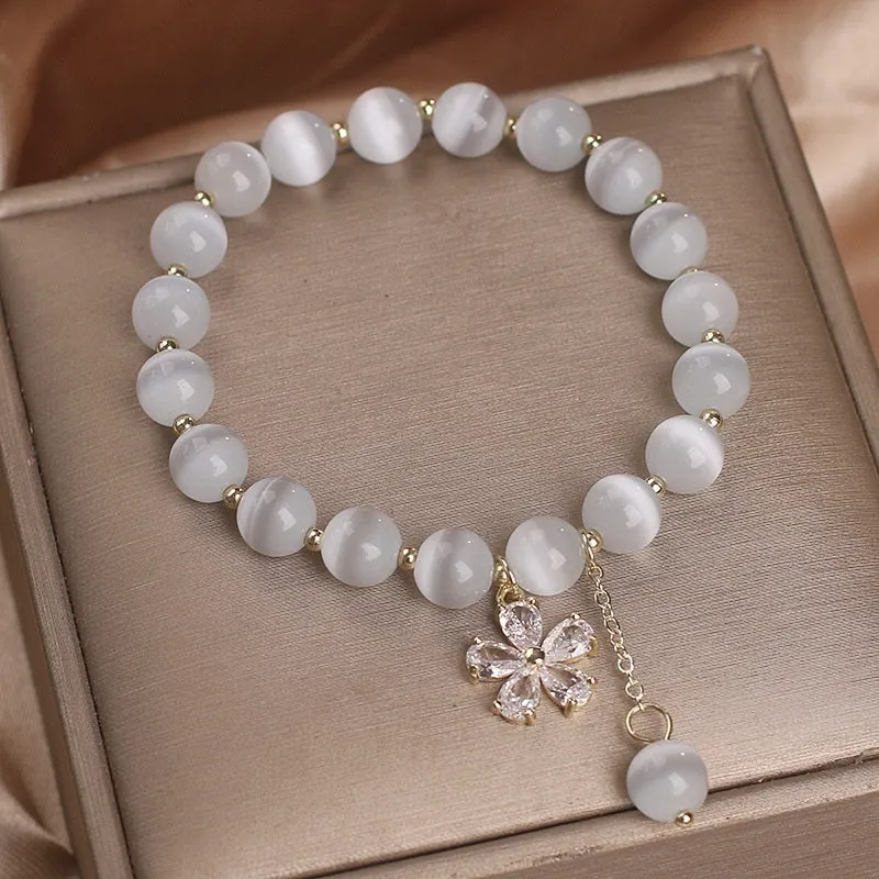 Close-up of a women's white cat's eye crystal bracelet with a flower tassel and silver safety buckle.