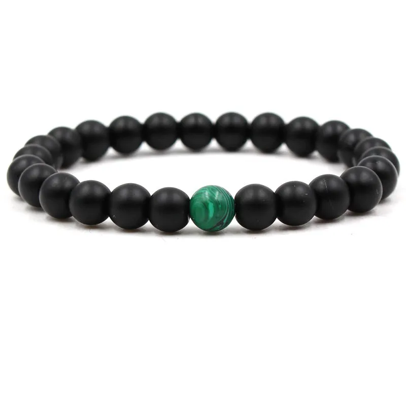 Malachite green and black matte 8mm round bead elastic strand bracelet on a neutral background
