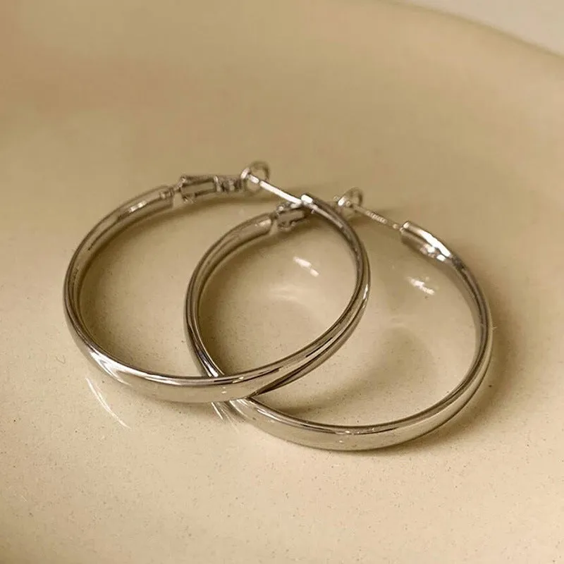 A pair of large, circular gold metal earrings against a plain background.