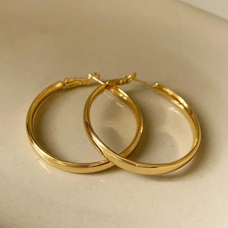 A pair of large, circular gold metal earrings against a plain background.