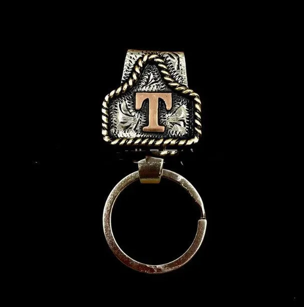 Handmade cow tag shaped metal keychain with a brown leather attachment strap.
