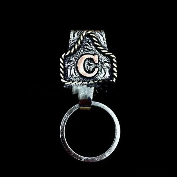 Handmade cow tag shaped metal keychain with a brown leather attachment strap.