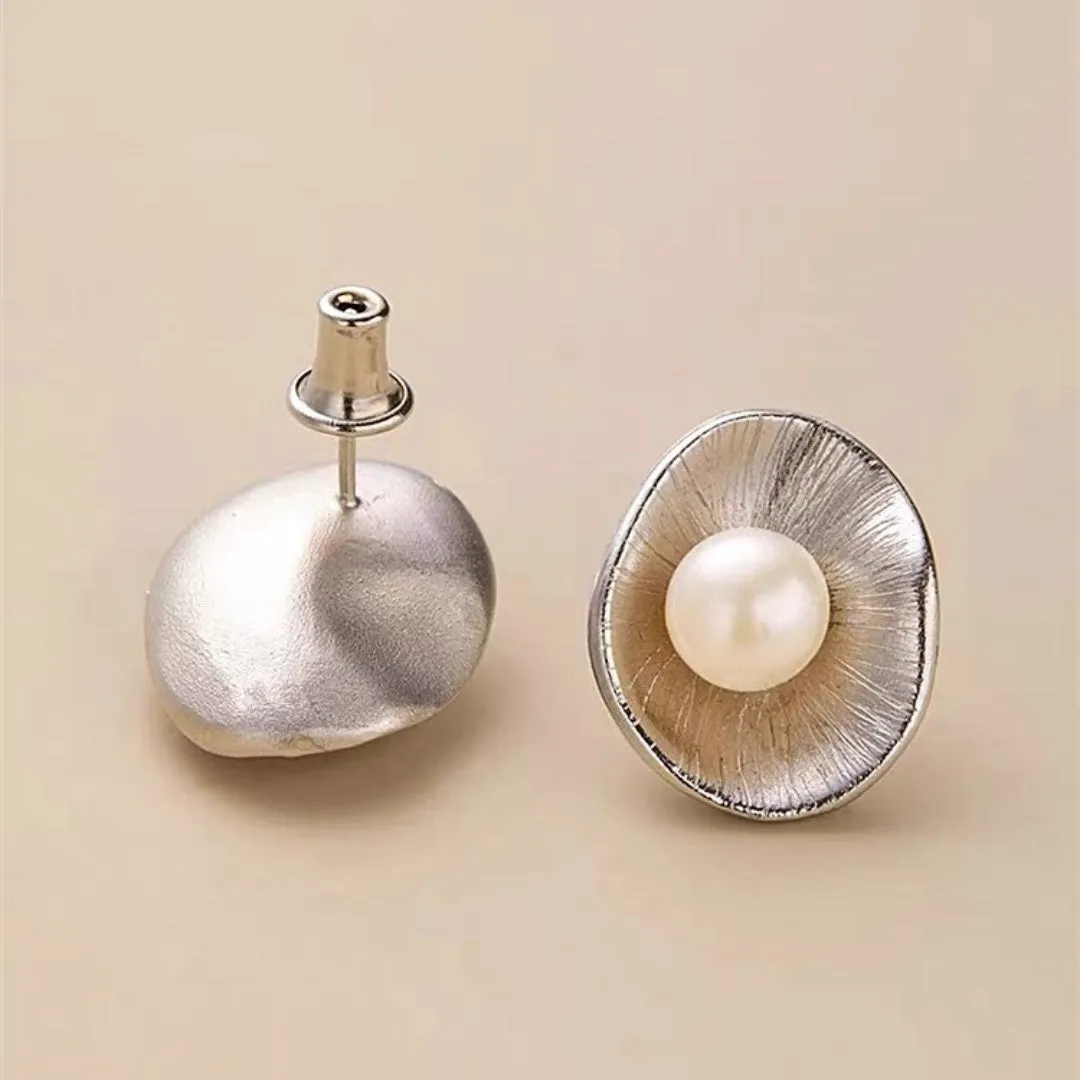 Gold tone geometric stud earrings with a central freshwater pearl on a silver needle post.