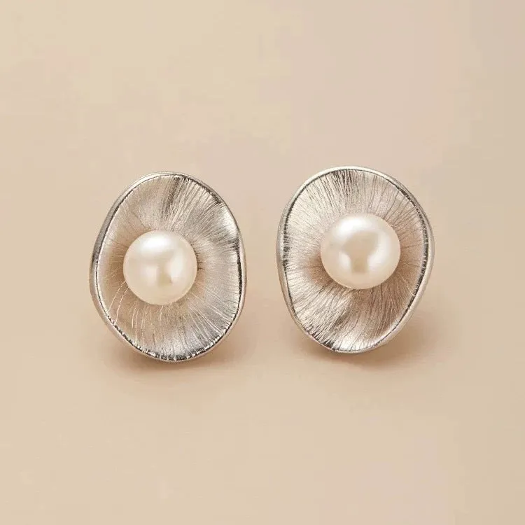 Gold tone geometric stud earrings with a central freshwater pearl on a silver needle post.