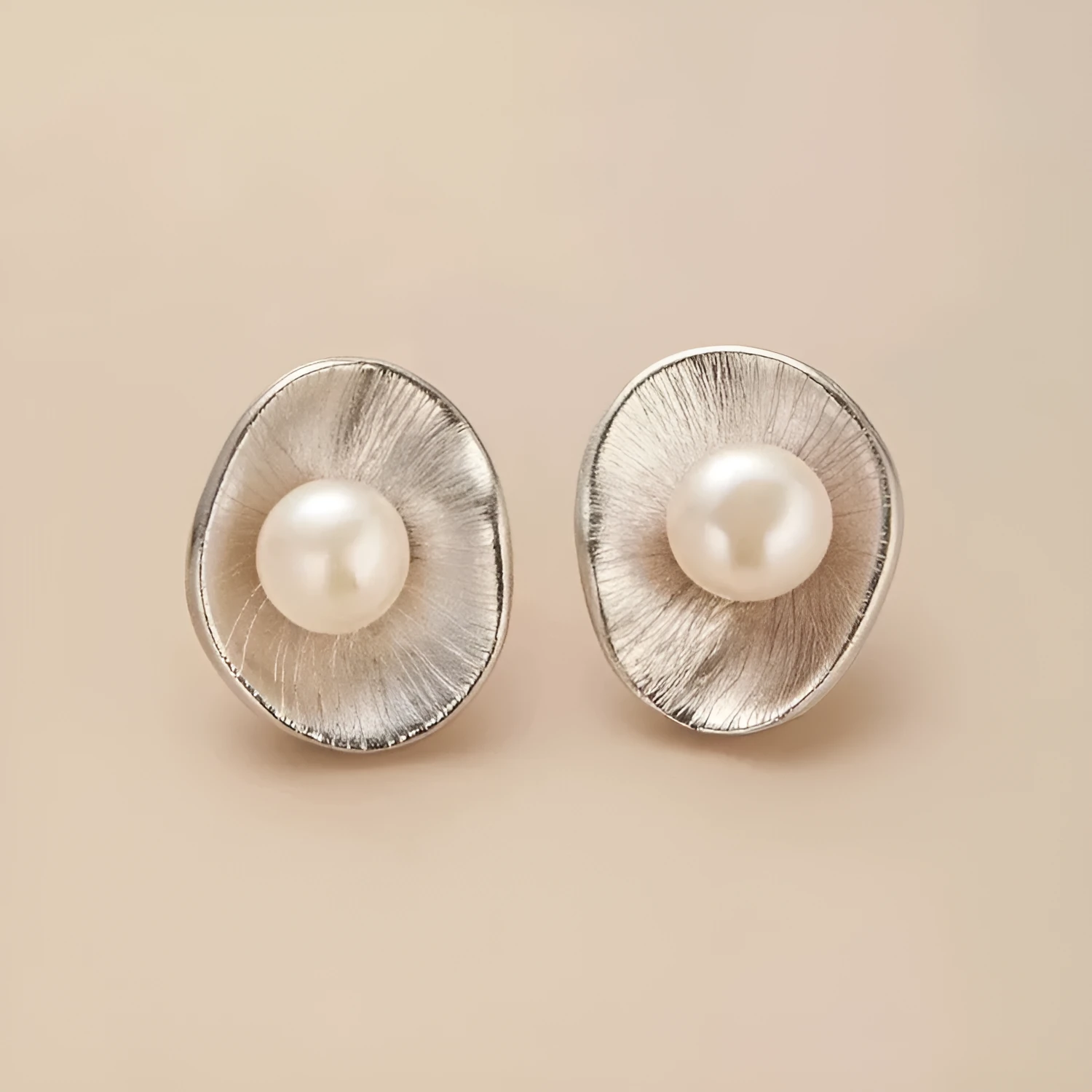 Gold tone geometric stud earrings with a central freshwater pearl on a silver needle post.