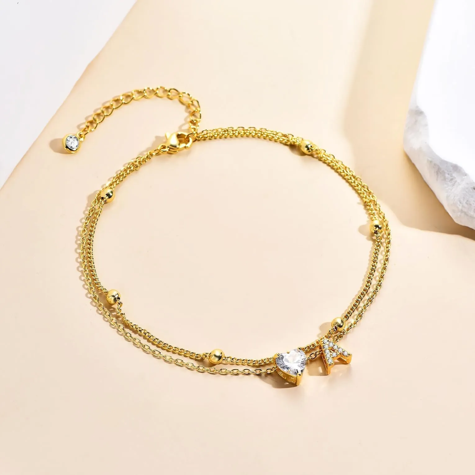 Layered copper anklet with zircon inlaid letter charm, bead zircon style, on a light background.