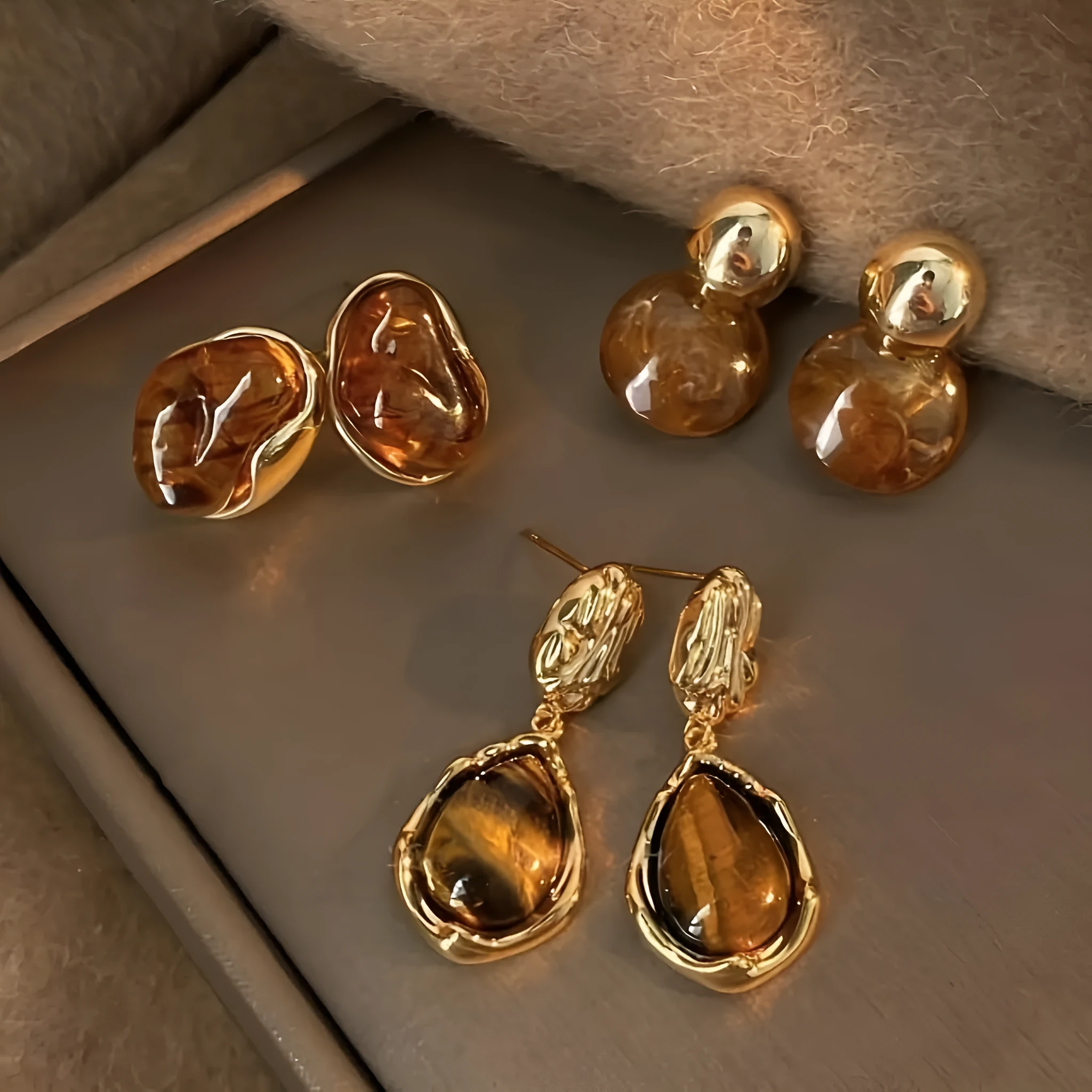 Three pairs of geometric tassel earrings in Maillard, amber, and tigereye colours on a white background