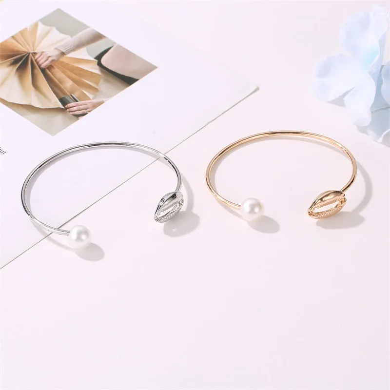 Alloy opening bracelet with pearl and shell decoration in gold finish on white background