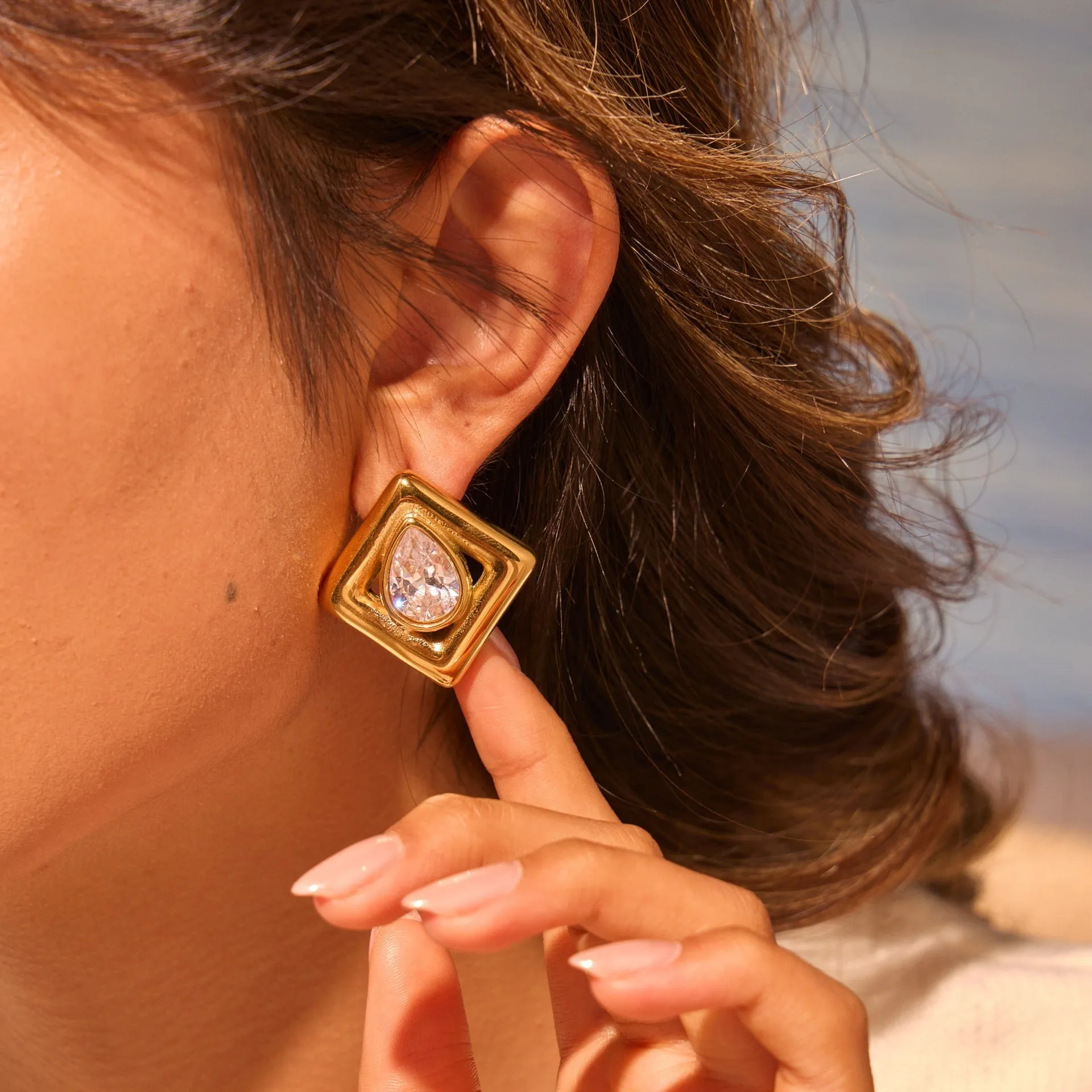 A pair of gold-coloured geometric stud earrings featuring an inlaid water drop zircon stone.