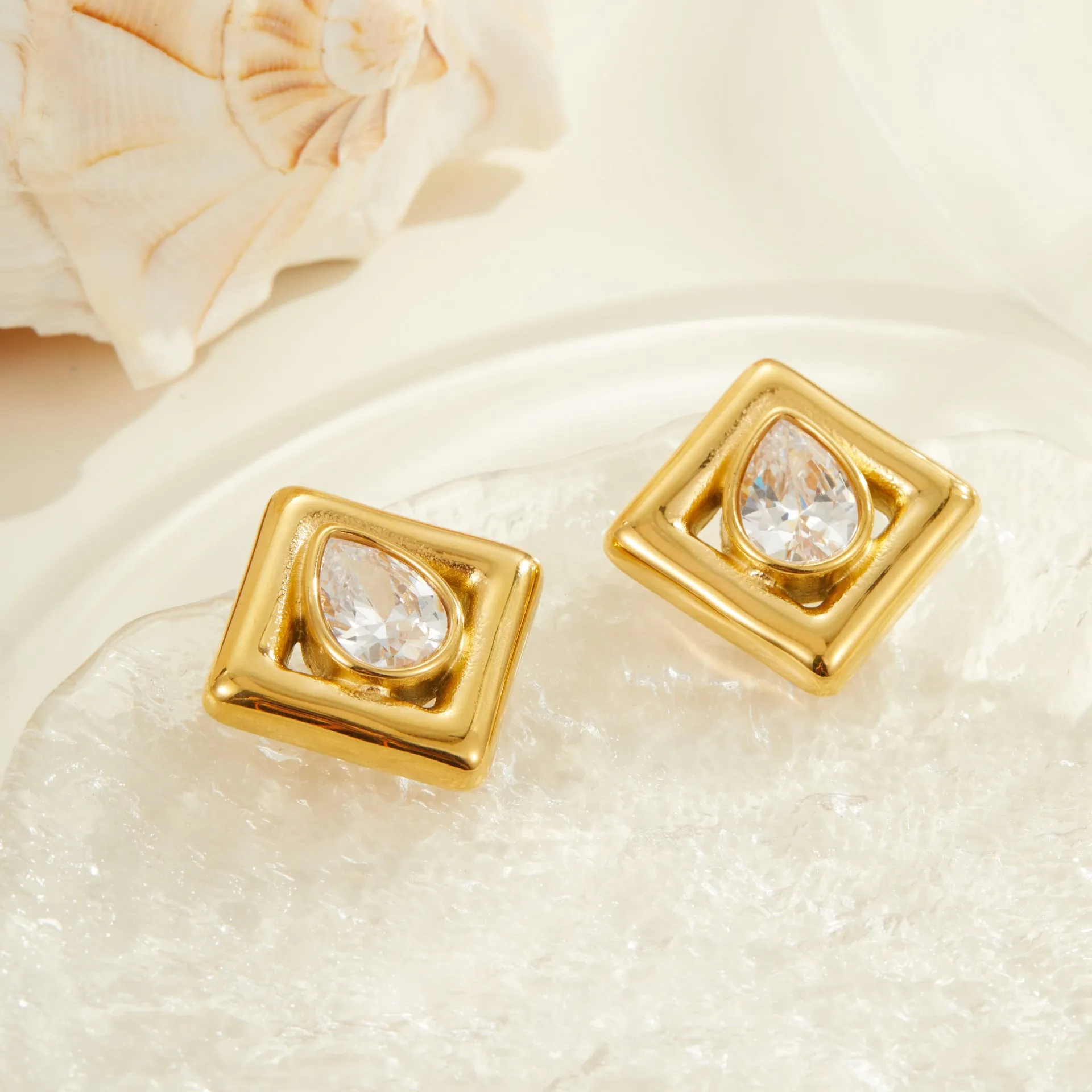 A pair of gold-coloured geometric stud earrings featuring an inlaid water drop zircon stone.