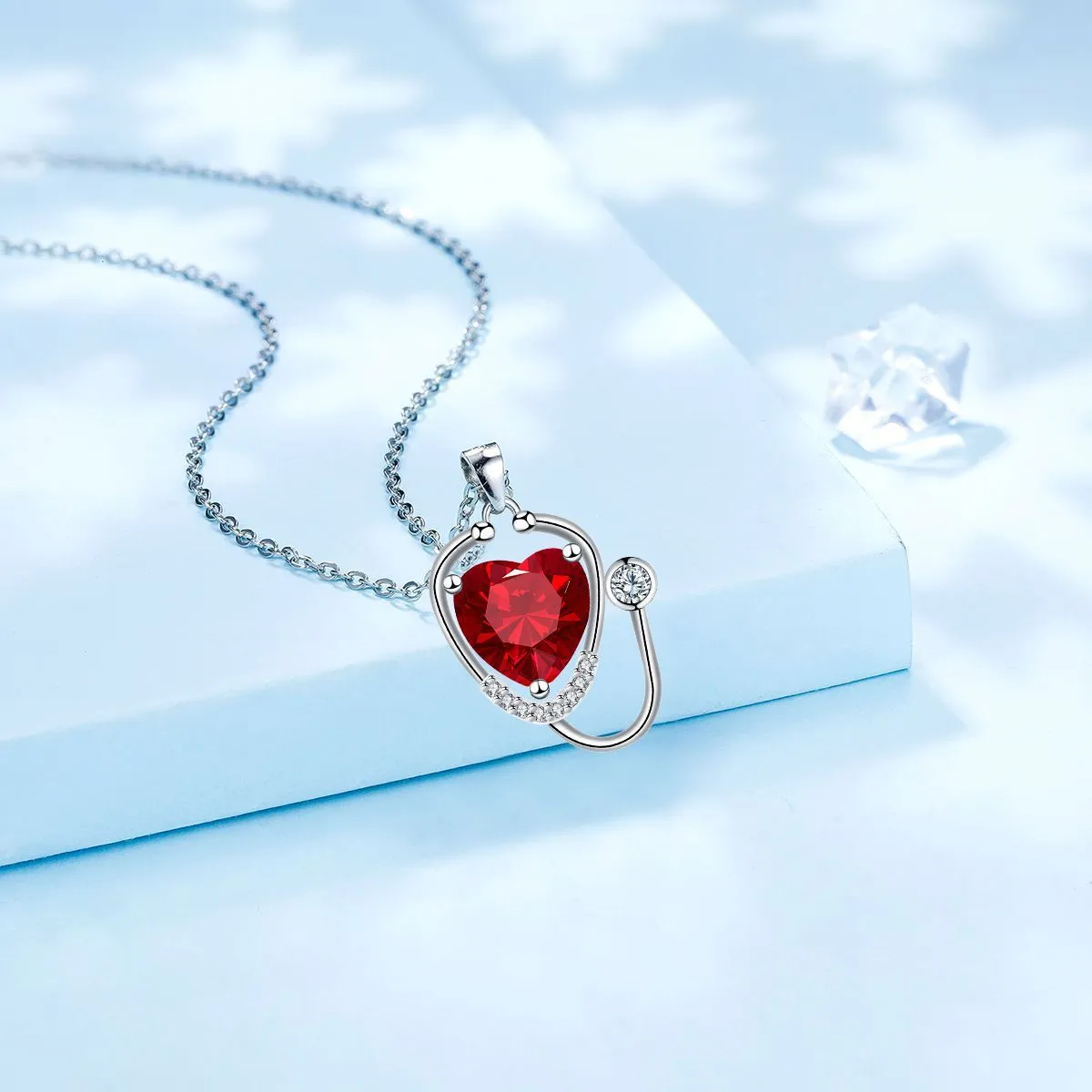Red diamond women's necklace with stethoscope, wing, and cross pendant design on a copper chain.