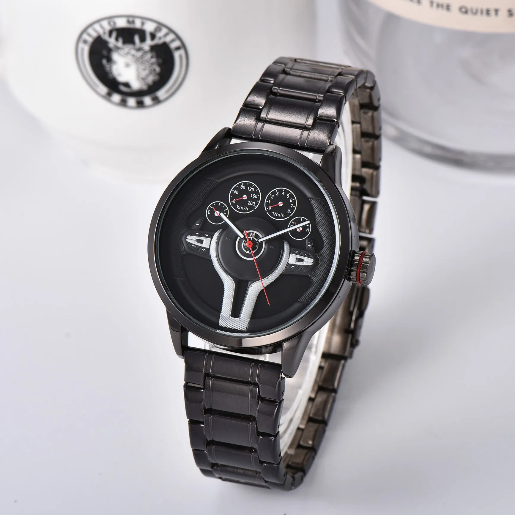 Steering wheel fashion watch with 43mm circular alloy case, stainless steel strap, and pointer display on a light background.