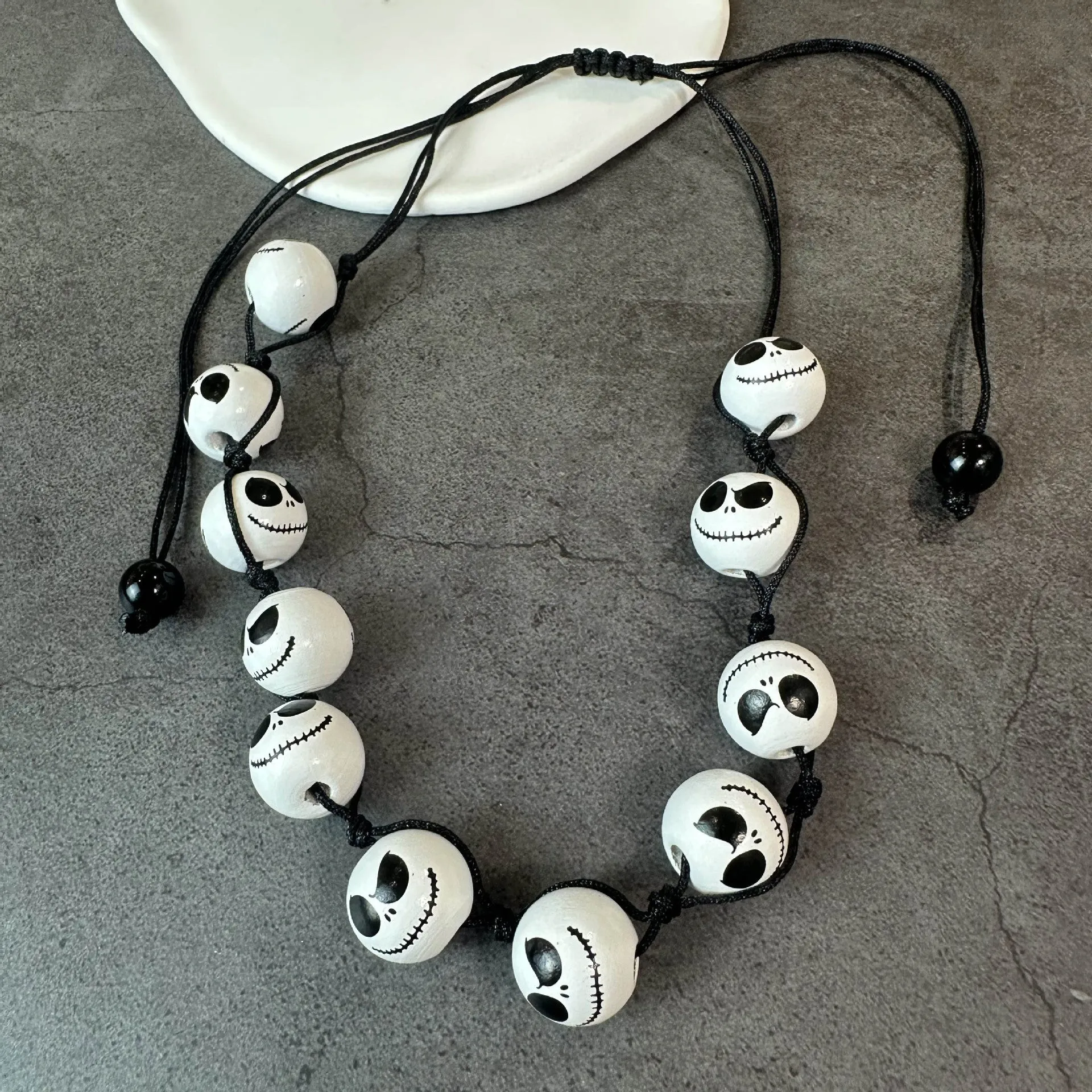 Handmade wooden bead Halloween jewellery set with ghost face, pumpkin, and skull motifs on a dark background.