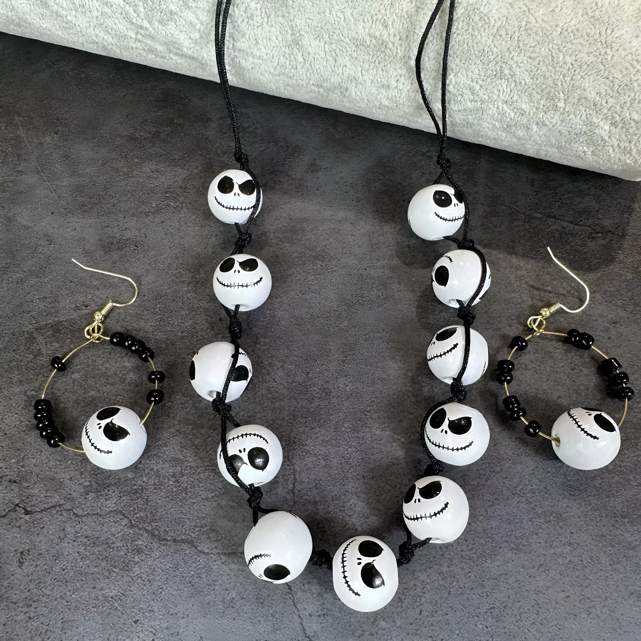 Handmade wooden bead Halloween jewellery set with ghost face, pumpkin, and skull motifs on a dark background.