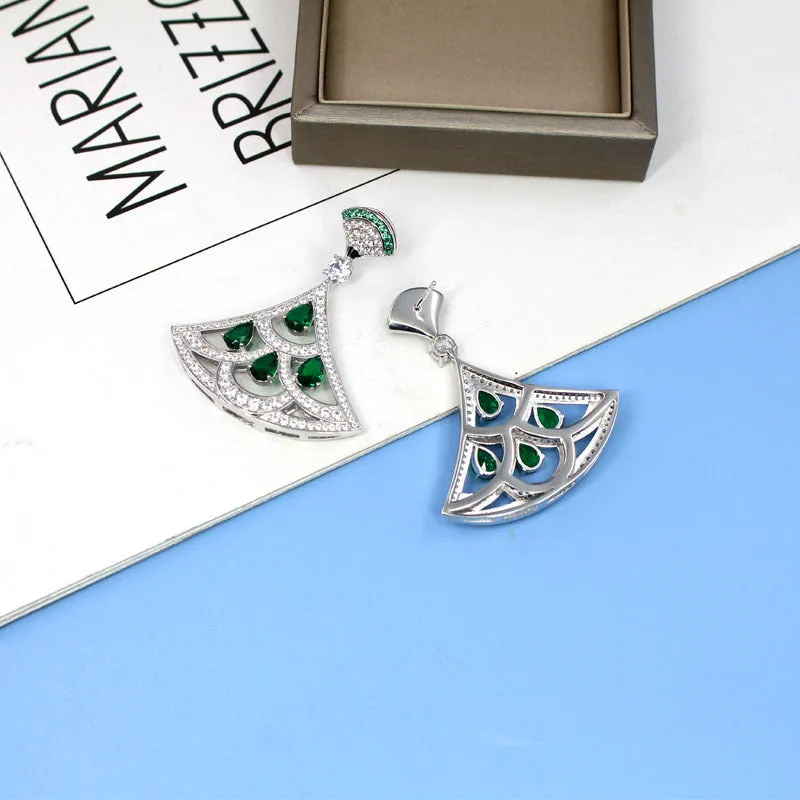 Silver fan-shaped earring with gold-plated inlay of artificial gems, on a plain background