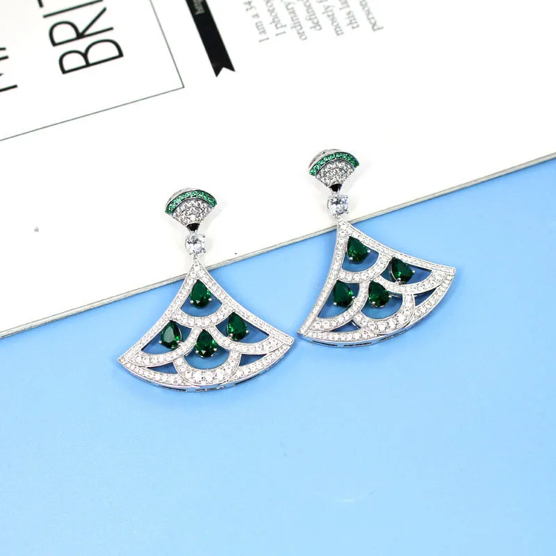 Silver fan-shaped earring with gold-plated inlay of artificial gems, on a plain background