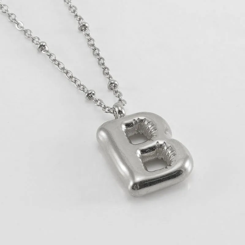 Gold bubble letter N pendant on stainless steel clip beads chain necklace against white background