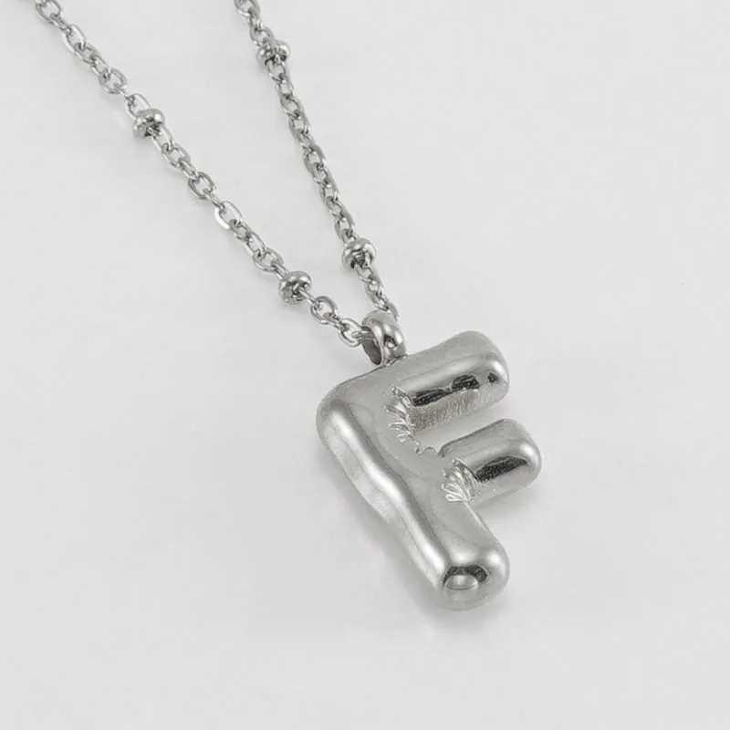 Gold bubble letter N pendant on stainless steel clip beads chain necklace against white background