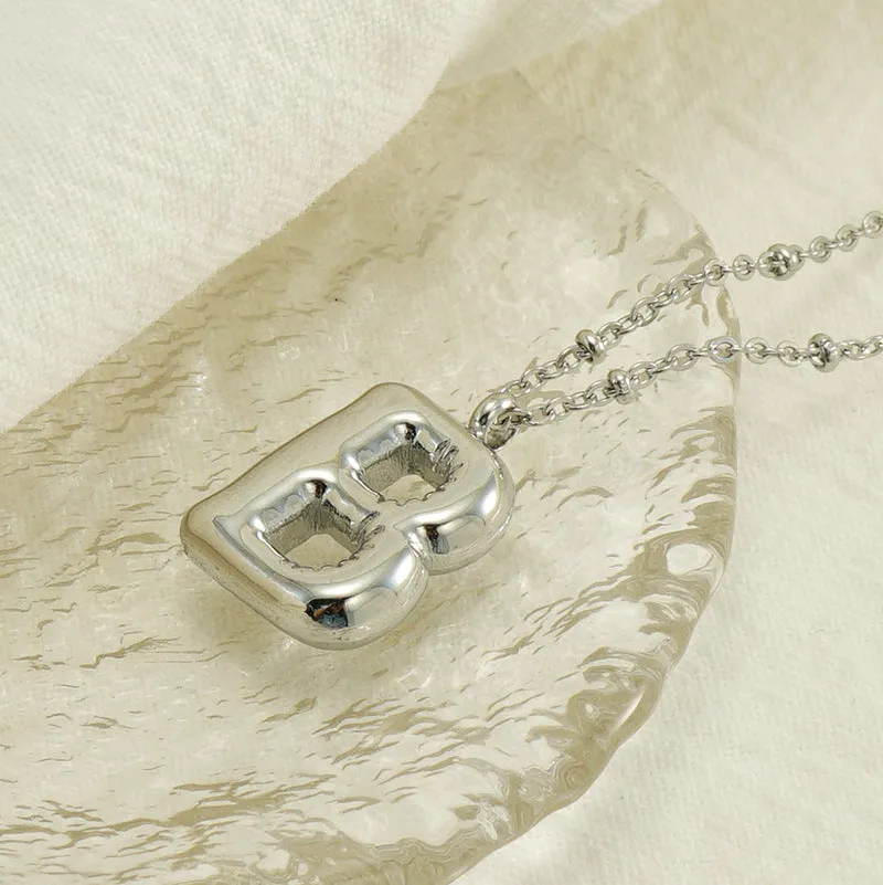 Gold bubble letter N pendant on stainless steel clip beads chain necklace against white background