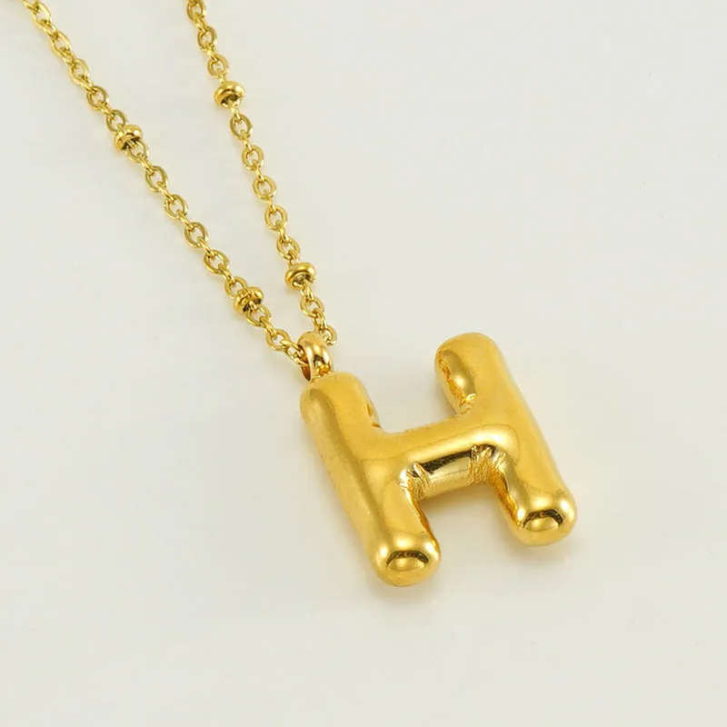 Gold bubble letter N pendant on stainless steel clip beads chain necklace against white background